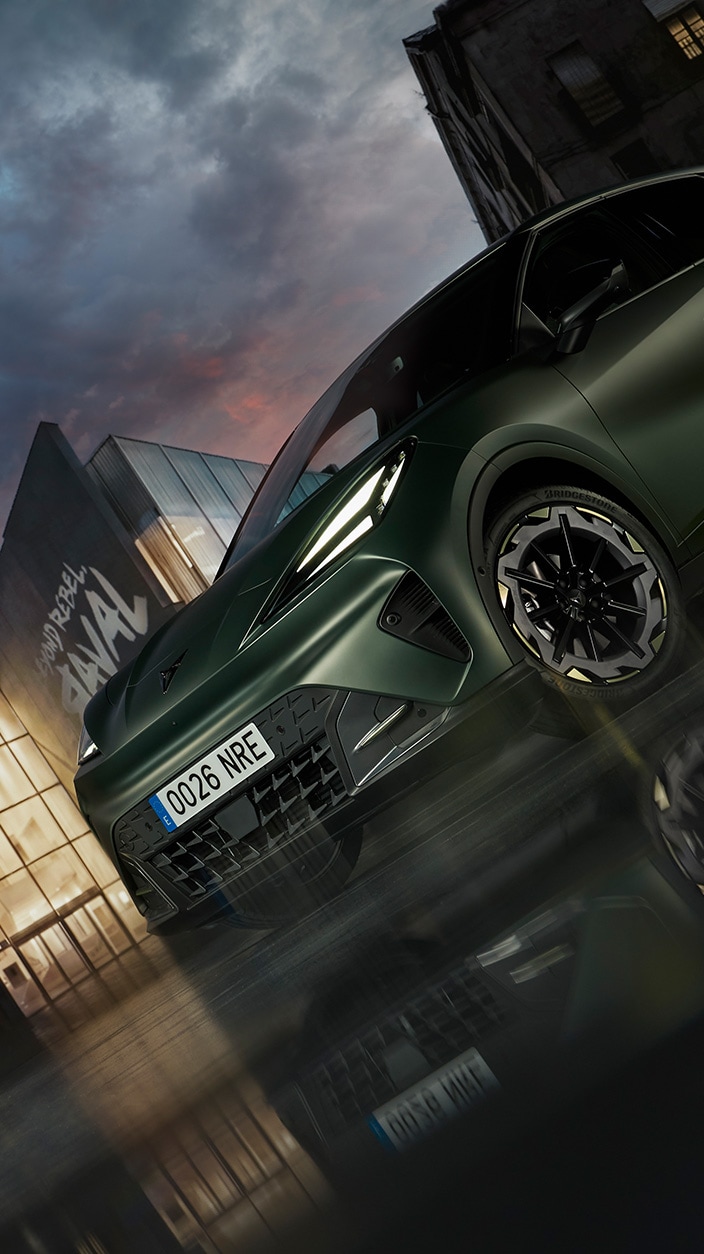 En CUPRA Raval parkert på en våt gate i skumringen, med høye leilighetsbygg opplyst i bakgrunnen.